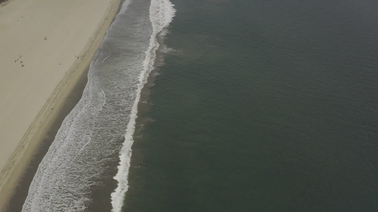 Overhead view of a Los Cabos beach where white surf foam runs diagonally beside dark green ocean water, with no visible people.