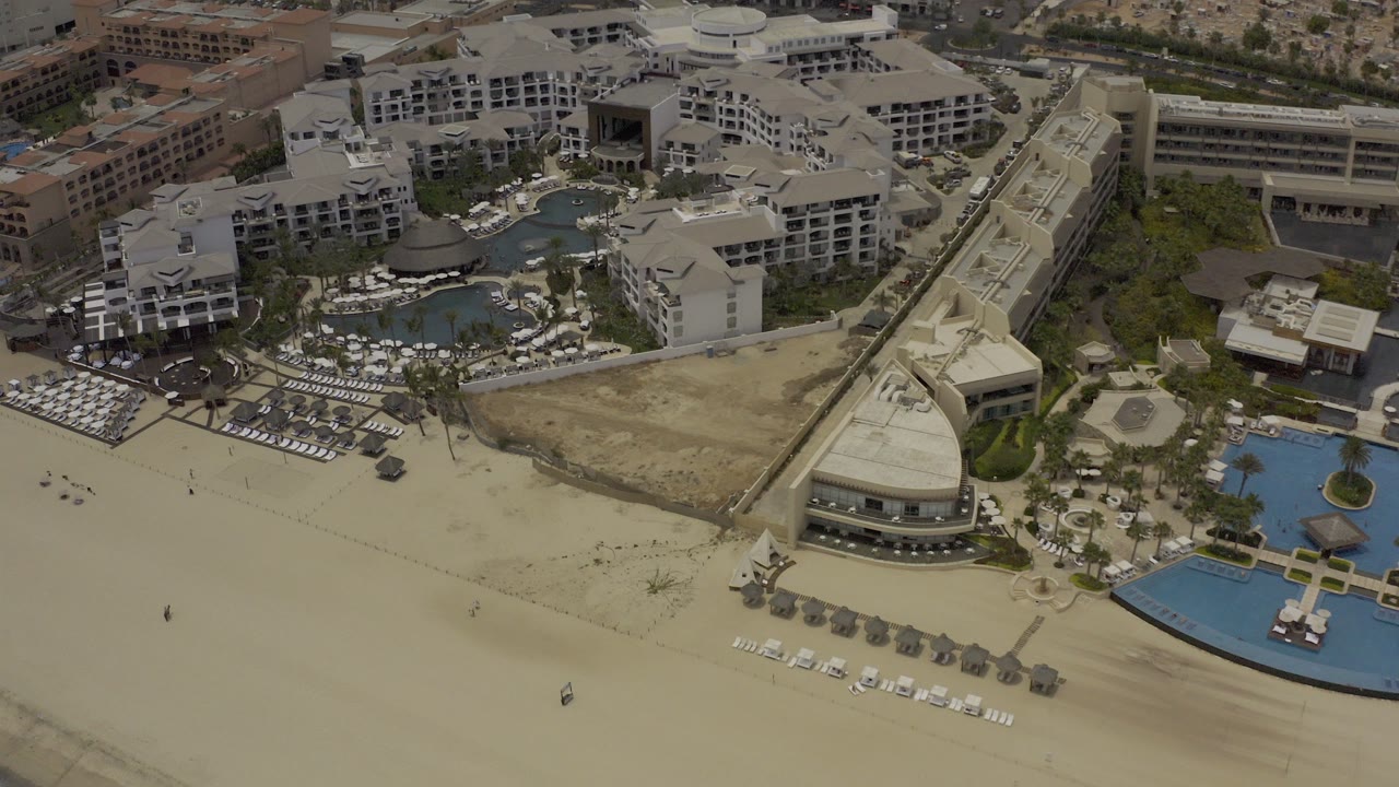 Aerial view of a beachfront resort with sand, pools, and hotel buildings.