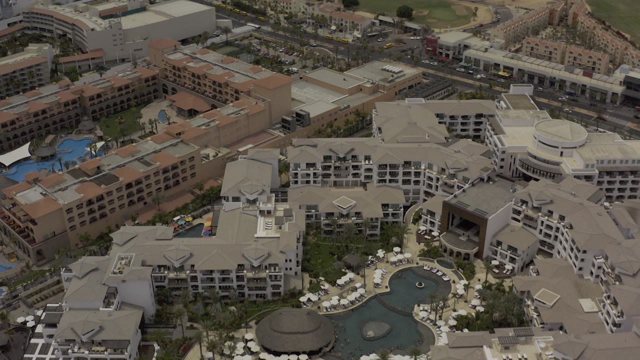 Aerial view of hotel buildings, pools, roads, and parked cars.