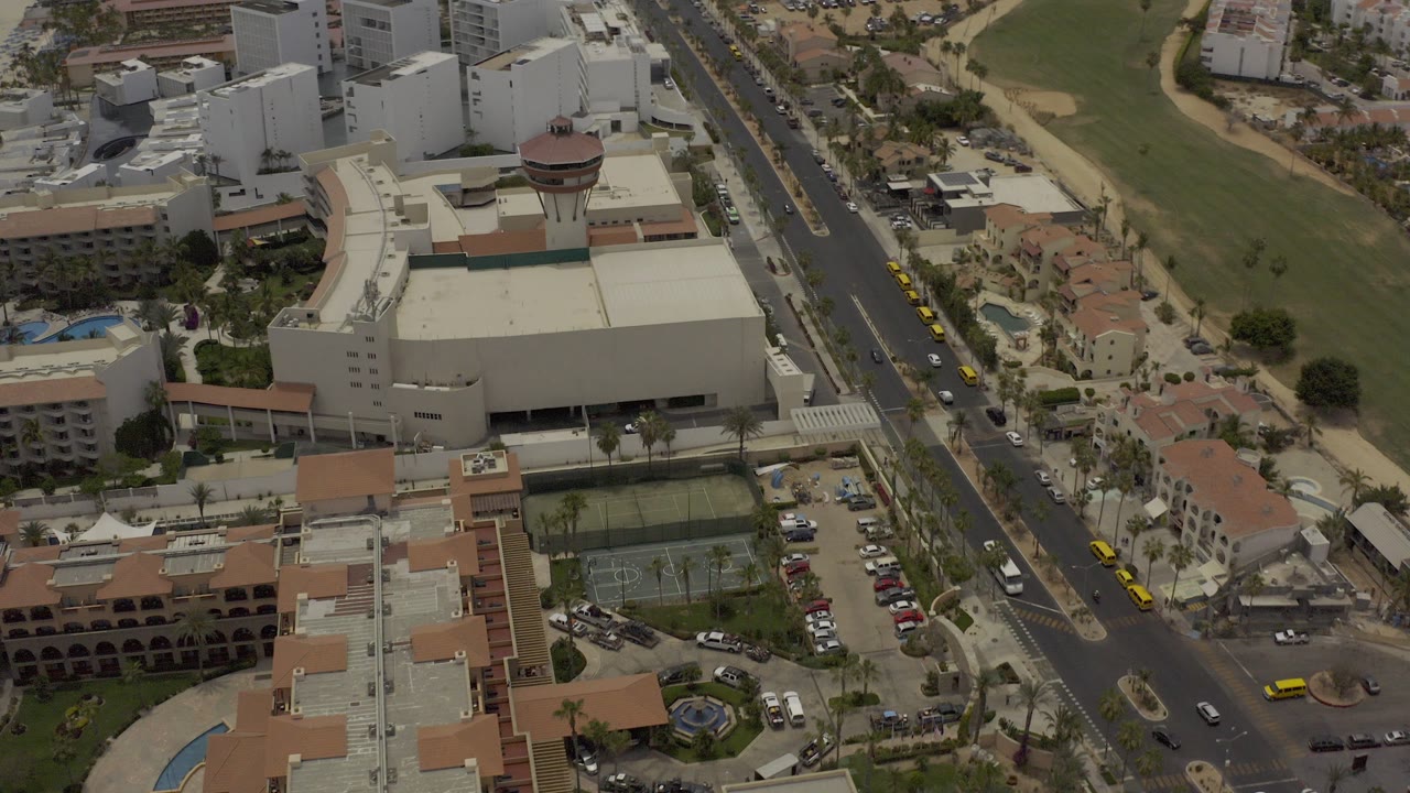 Aerial view of large buildings, a divided road, tennis courts, and parking areas.