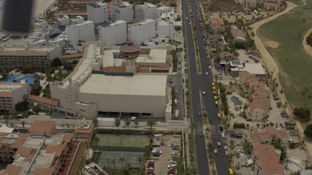 Aerial city block with traffic, large buildings, pools, and golf-like green space.