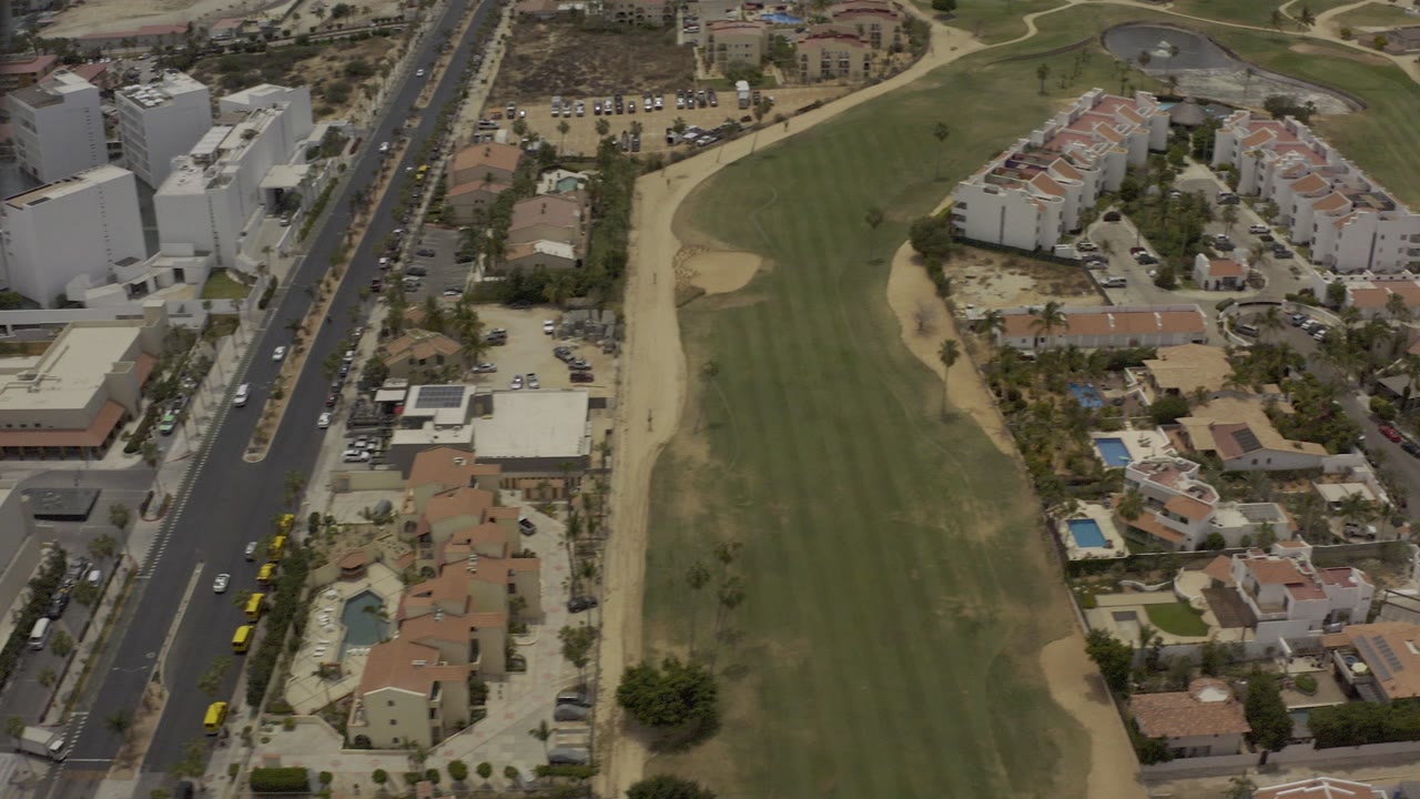Overhead view of a green field beside a highway and residential buildings.