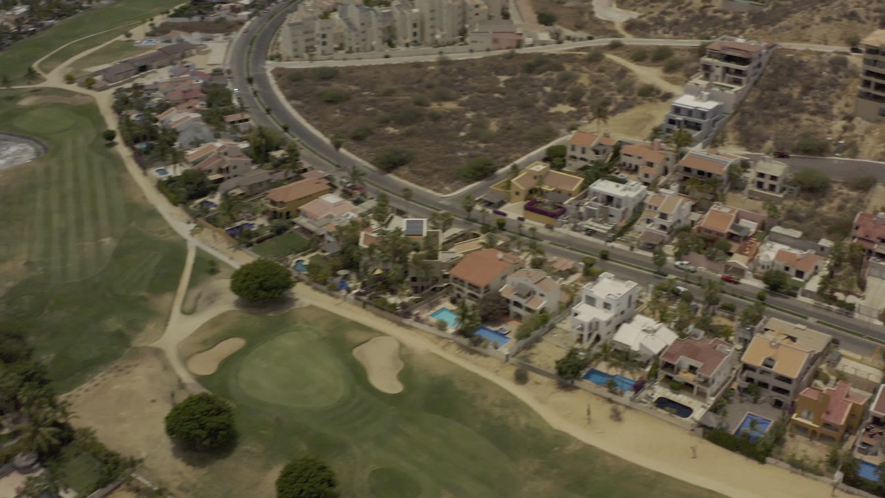 Aerial view of golf course greens beside suburban homes and roads.