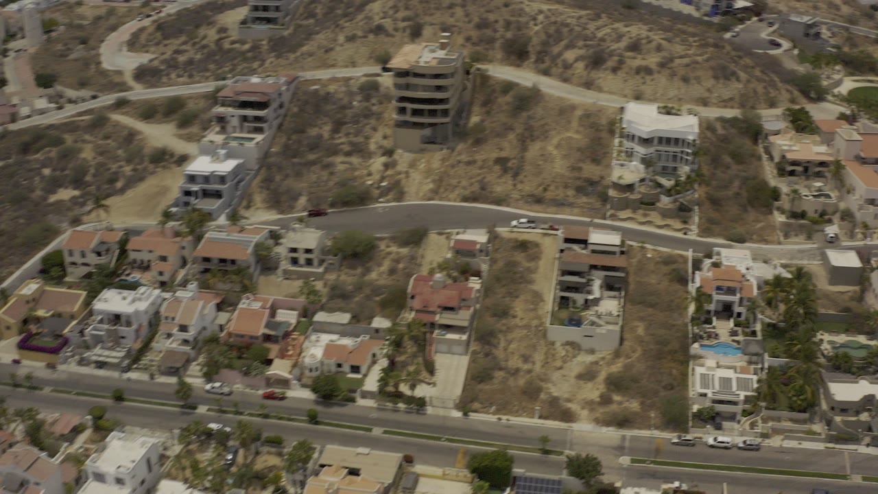 Aerial view of hillside homes and dry terrain beside a curving road.