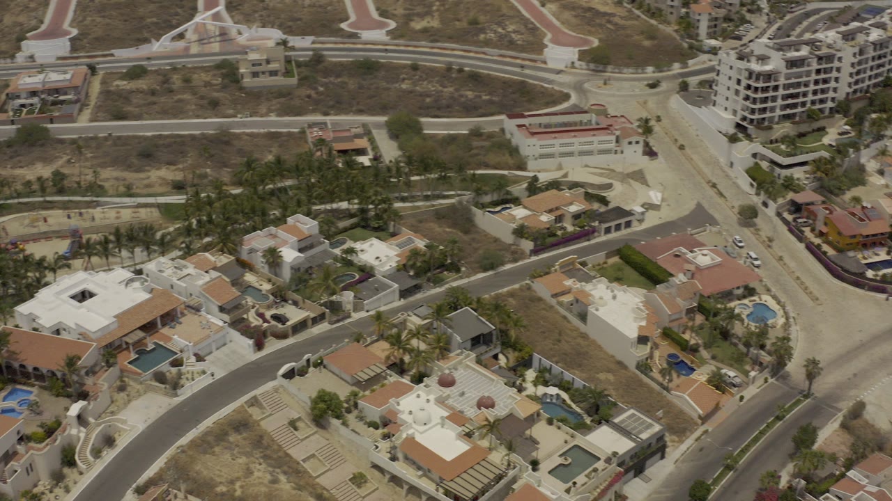 Aerial view of residential roads, villas, pools, palms, and dry hillside lots.