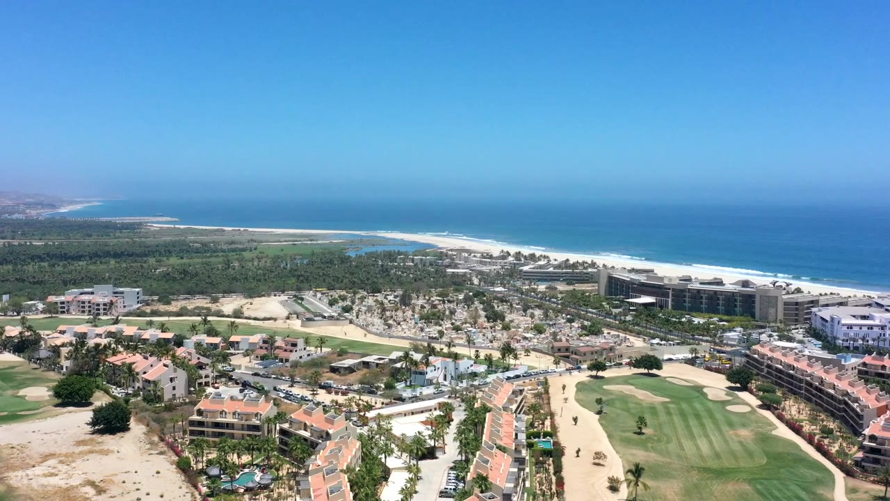 Aerial coastal view with buildings, golf course, lagoon, beach, and ocean.