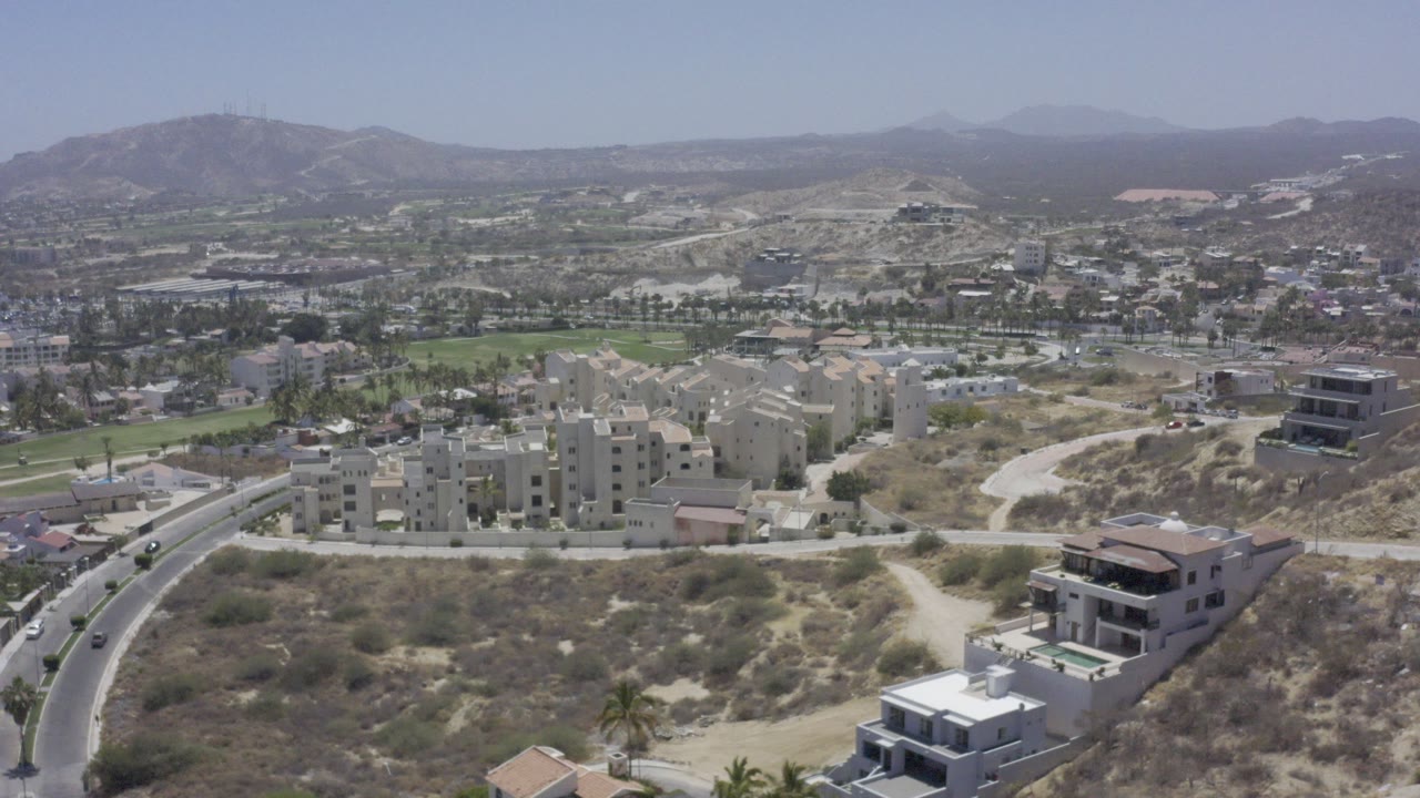 Aerial view of Los Cabos buildings, road, desert lots, and mountains.