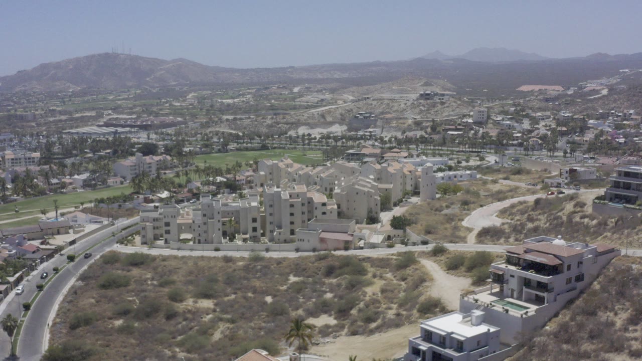 Aerial view of hillside roads, apartment buildings, green fields, and distant mountains.