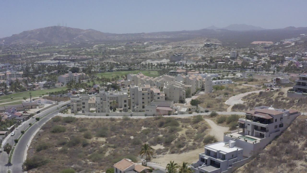 Aerial view of hillside buildings, curved road, dry lots, and distant mountains.