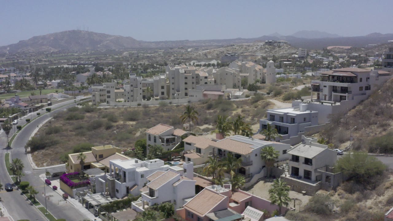 Aerial view of hillside homes, streets, palms, and distant mountains.