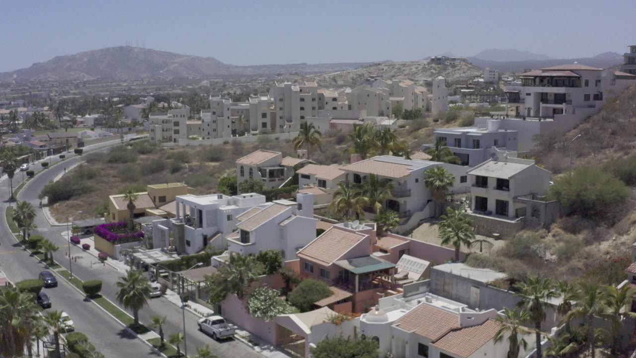 Elevated view of hillside homes, palm trees, road, and distant hills.