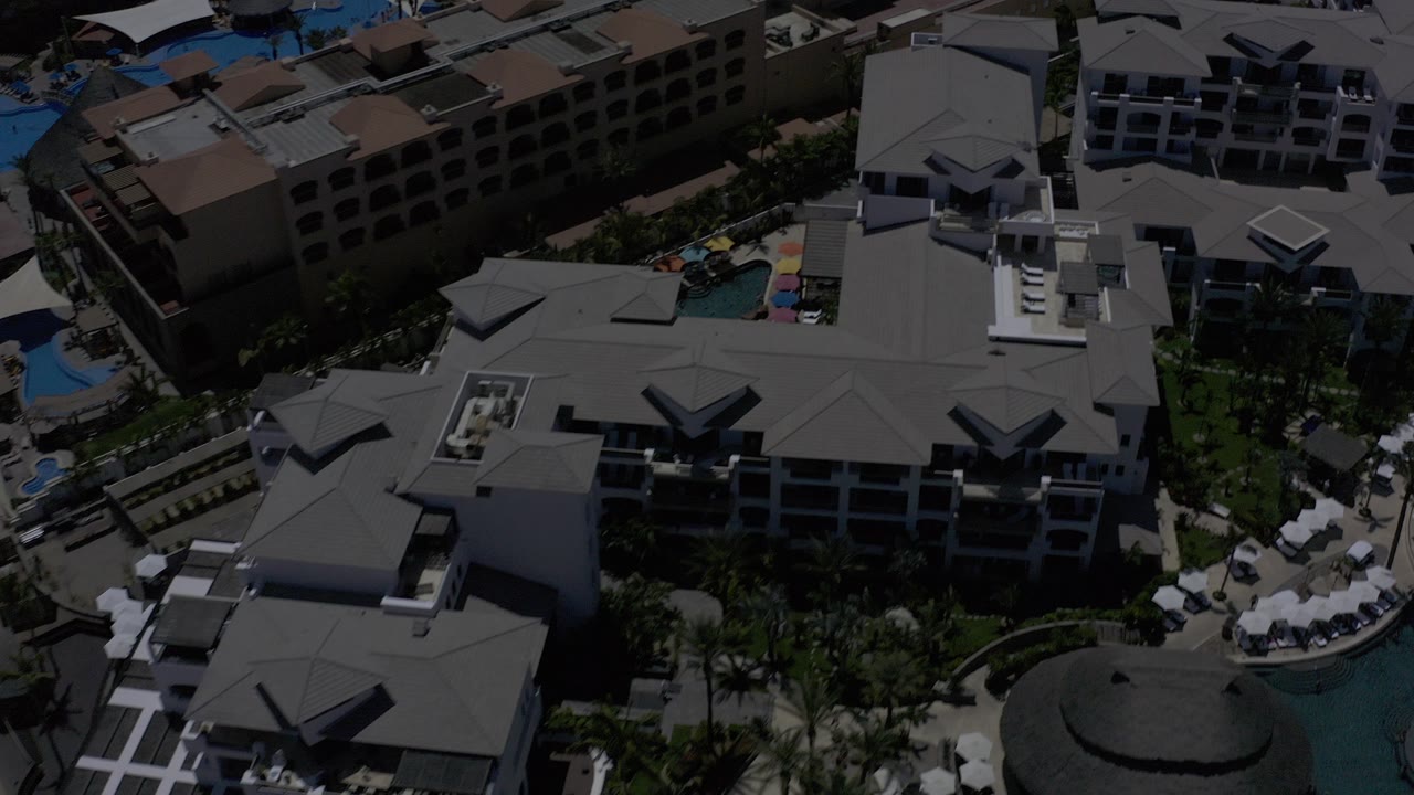 Aerial view of resort buildings, pools, palms, and umbrellas.