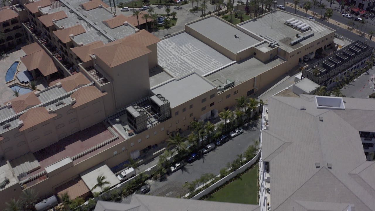 High aerial view of mall rooftops, palm-lined streets, and parked cars.