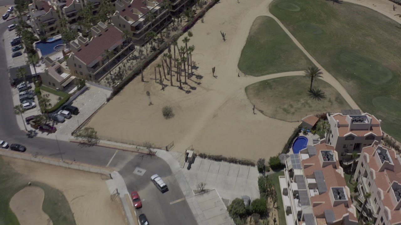Aerial view of houses, road, sand, palms, and green turf.