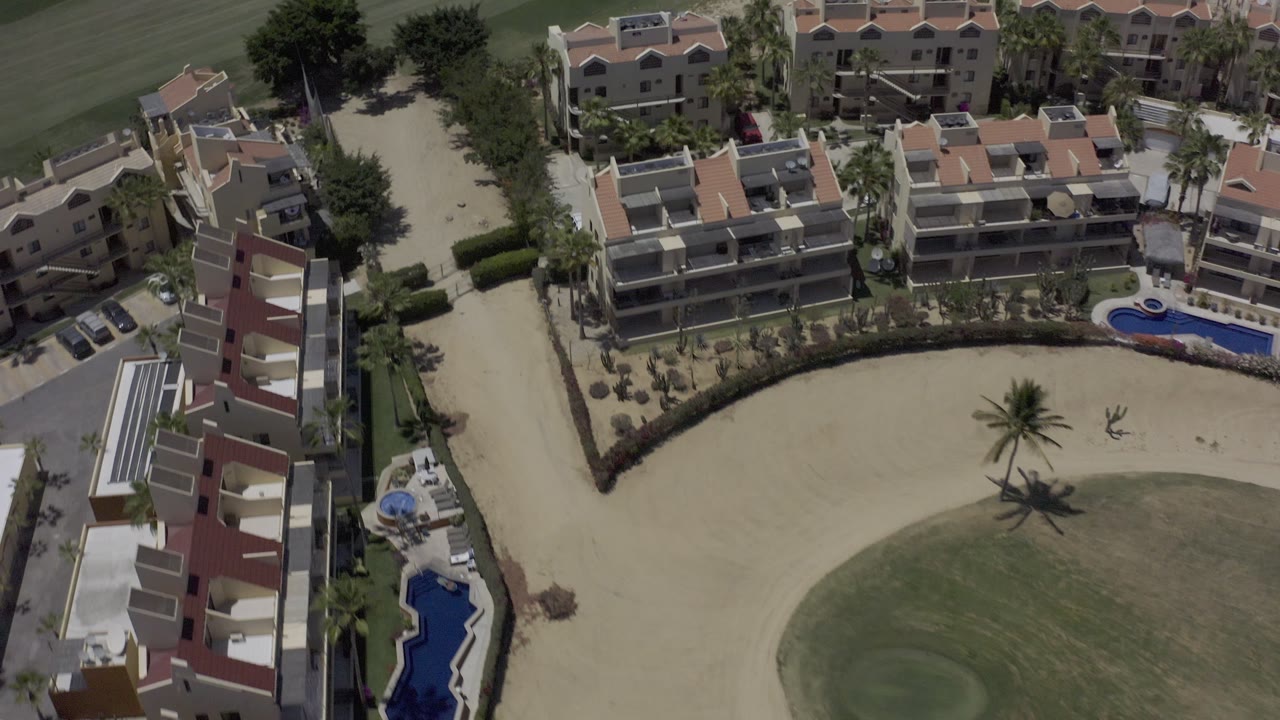 Aerial view over apartment-style rentals, a pool edge, palms, and golf course.