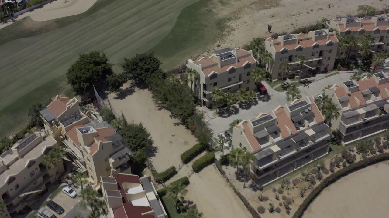 Aerial view of tile-roofed buildings beside a golf fairway and sand trap.