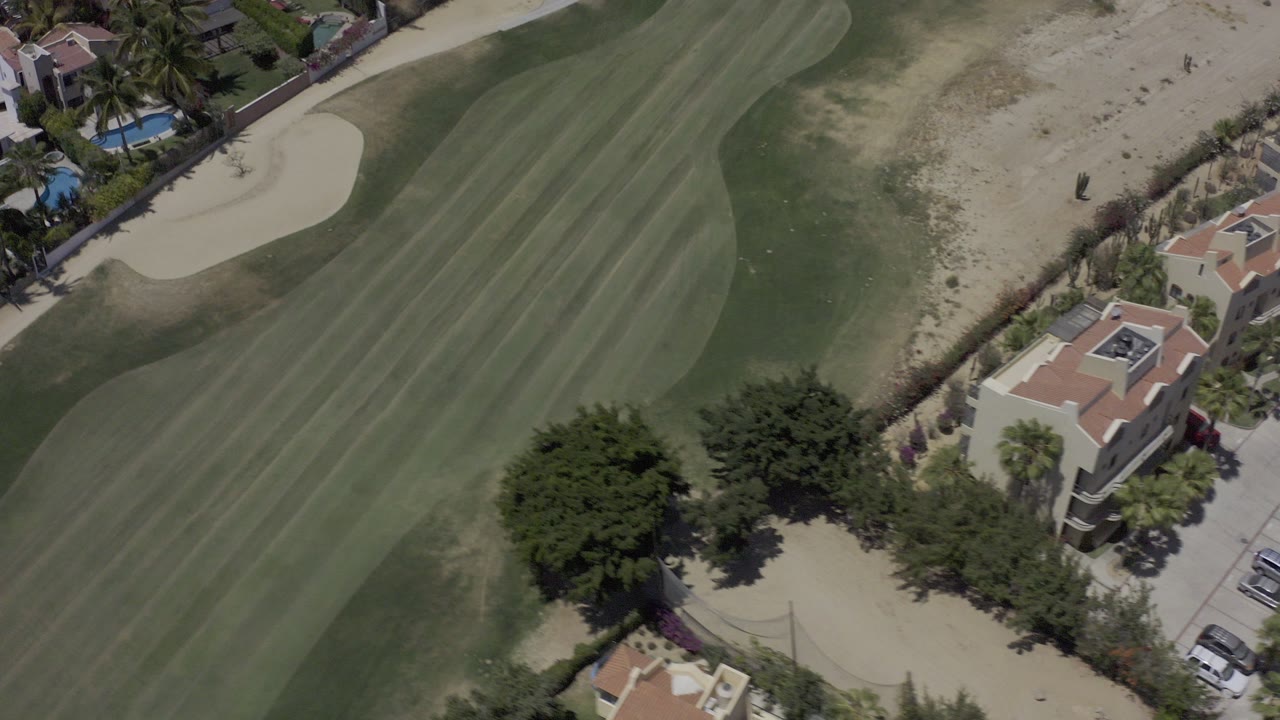 Overhead view of a golf fairway beside homes and sand bunkers.