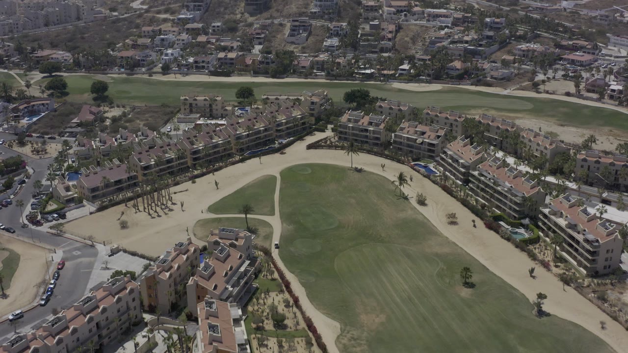 Drone view over a green field and surrounding residential buildings.
