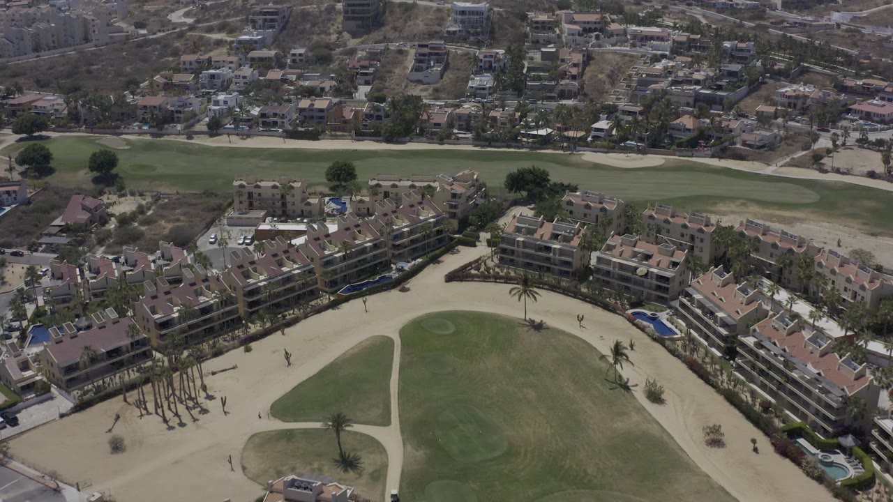 Aerial view of fairway, sand, palm trees, and surrounding buildings.