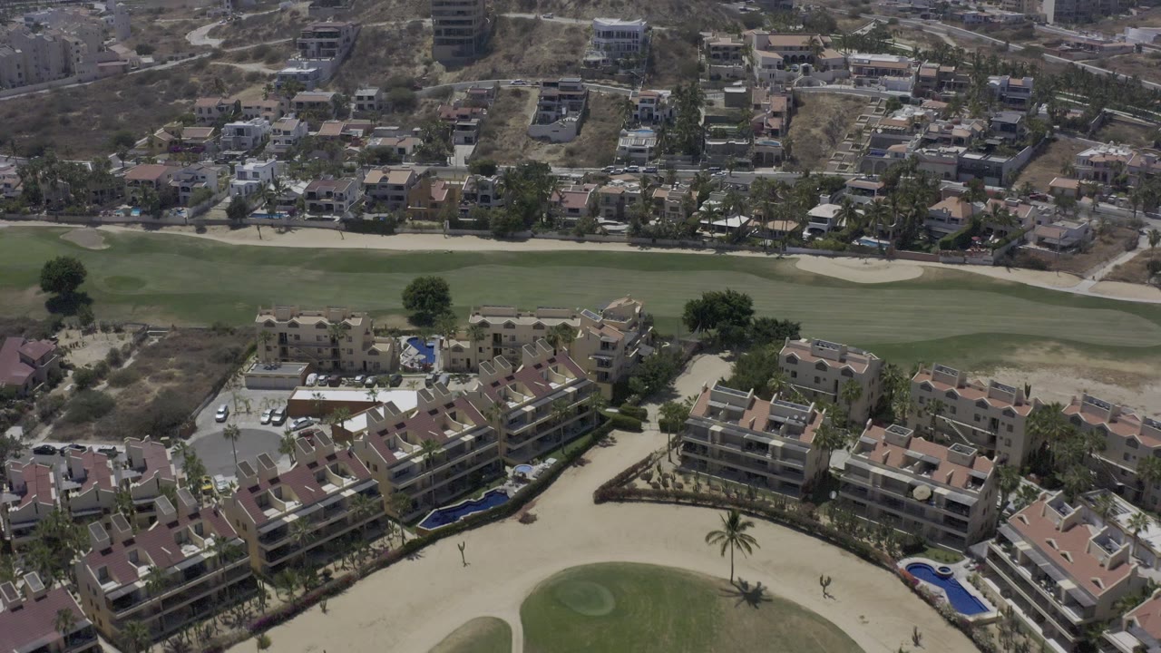 Overhead view of Los Cabos condos with a golf green and homes beyond.