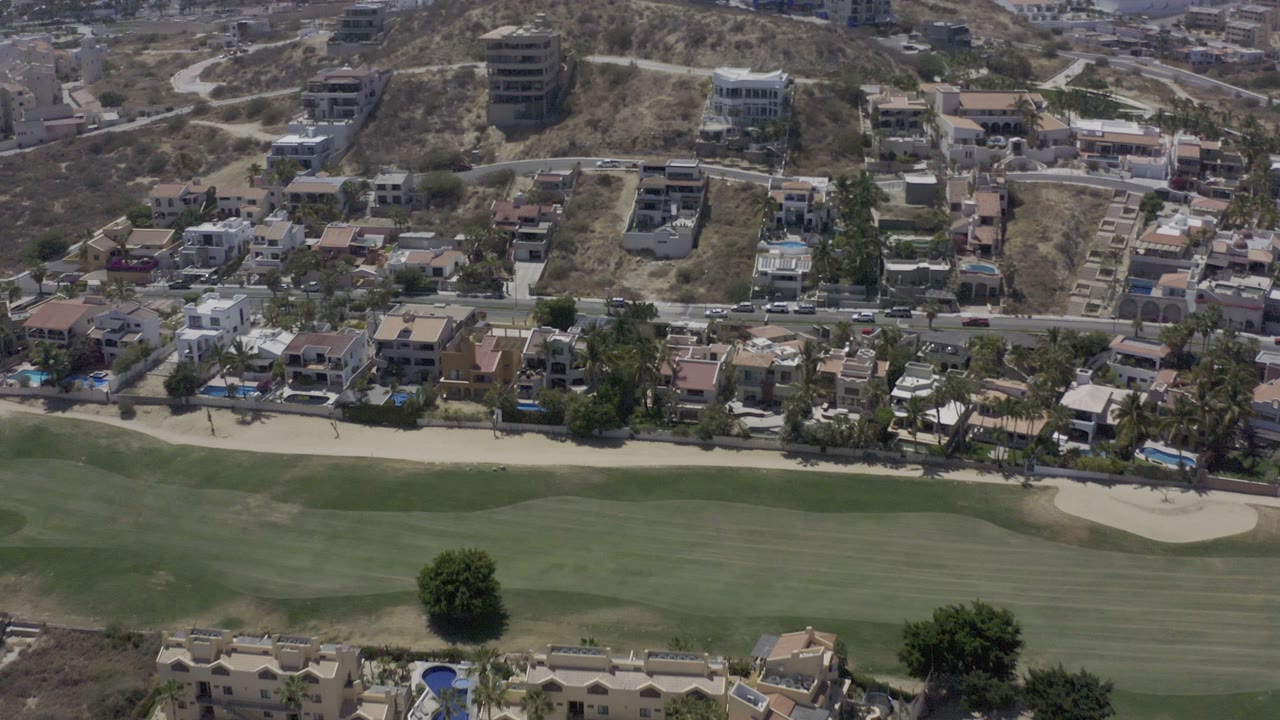 Aerial view of a golf fairway, homes, road, and dry hillside.