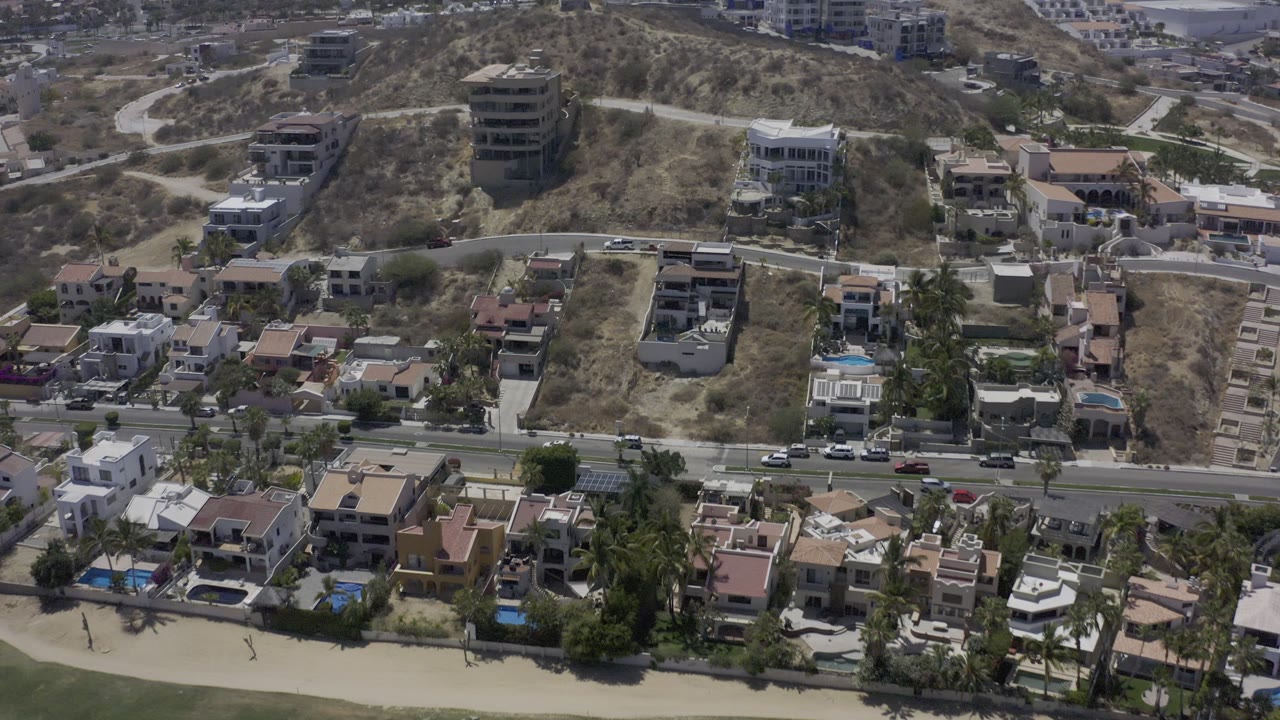 Drone view over beachside houses, road traffic, and dry slopes