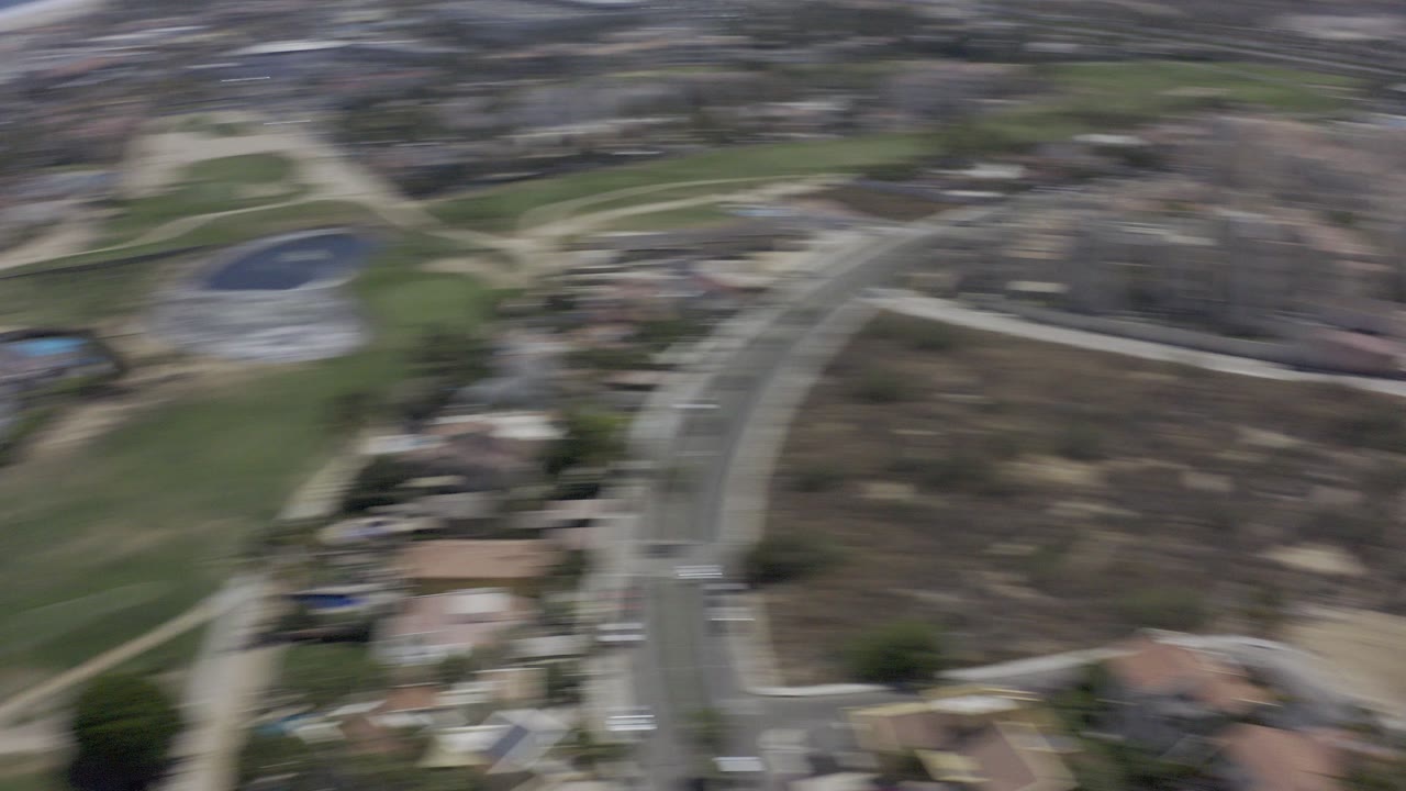 Blurred aerial view over roads, homes, green grounds, and water