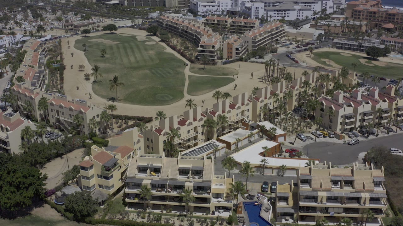 Overhead view of resort buildings beside golf-course greens and sandy paths.