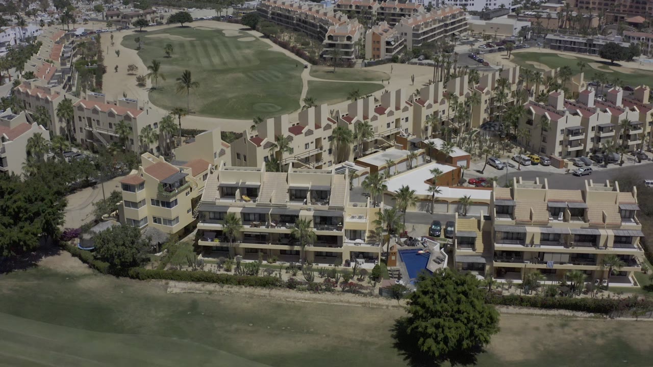 Elevated Los Cabos resort view with a broad green fairway in front, layered hotel blocks behind it, and no visible people.