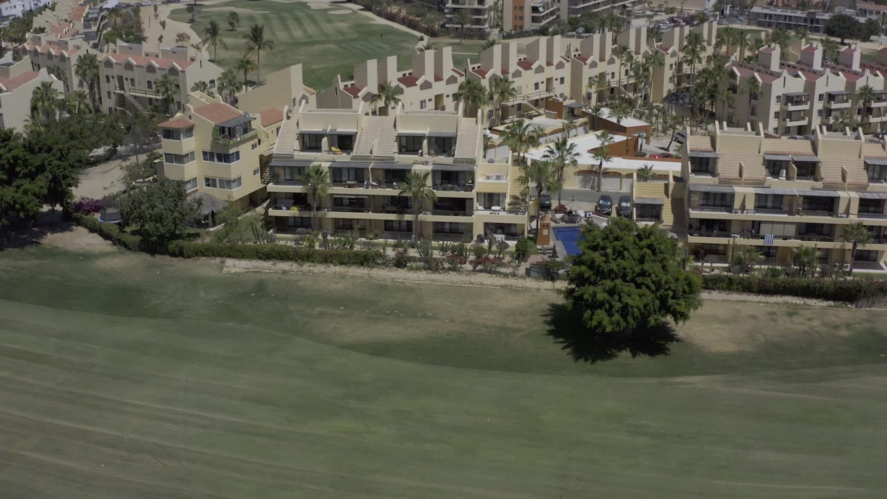 Golf course grass stretches below buildings with palms and landscaping.
