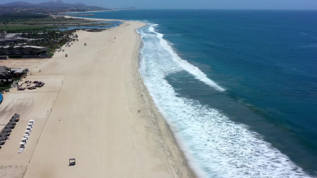 Bird's-eye coastline view with waves rolling onto a long beach.