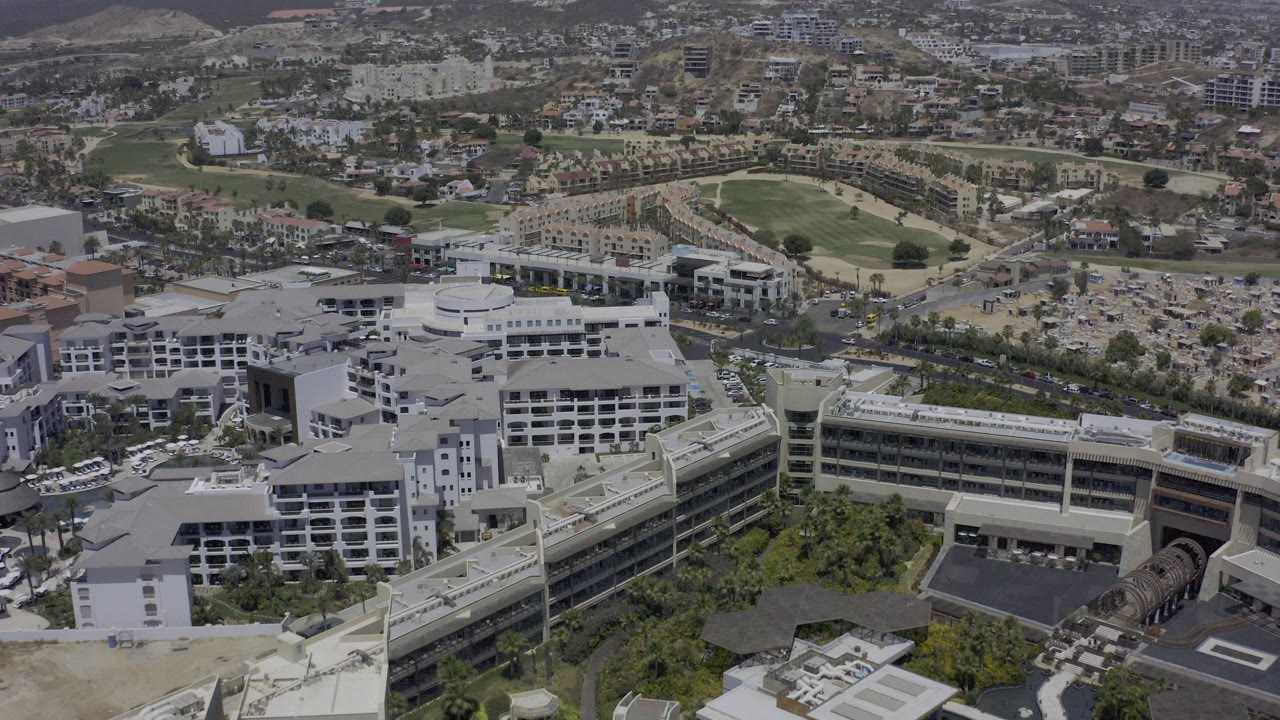 Aerial view over white multi-story buildings with roads, parking areas, and a distant green track.