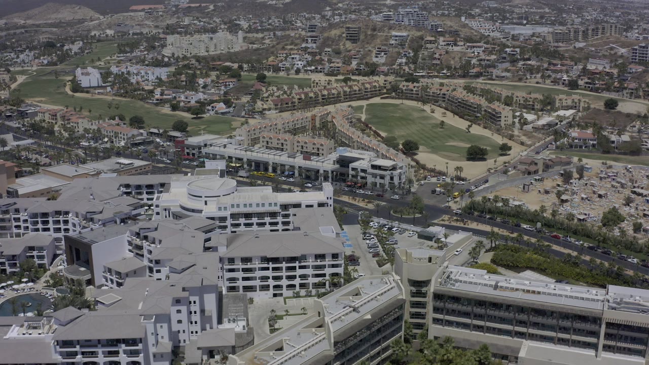 Aerial city view with large white buildings, road traffic, golf greens, and construction areas.