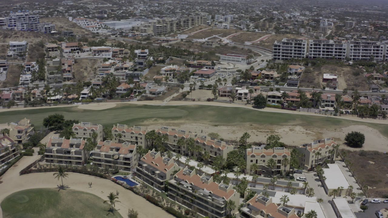 Aerial view of condos, golf greens, sandy bunkers, roads, and hillside buildings.