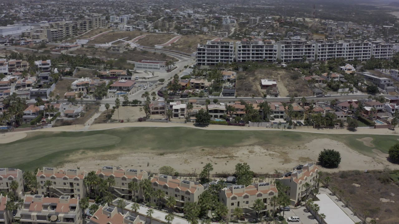 Aerial view over condos, streets, dry lots, and green turf.
