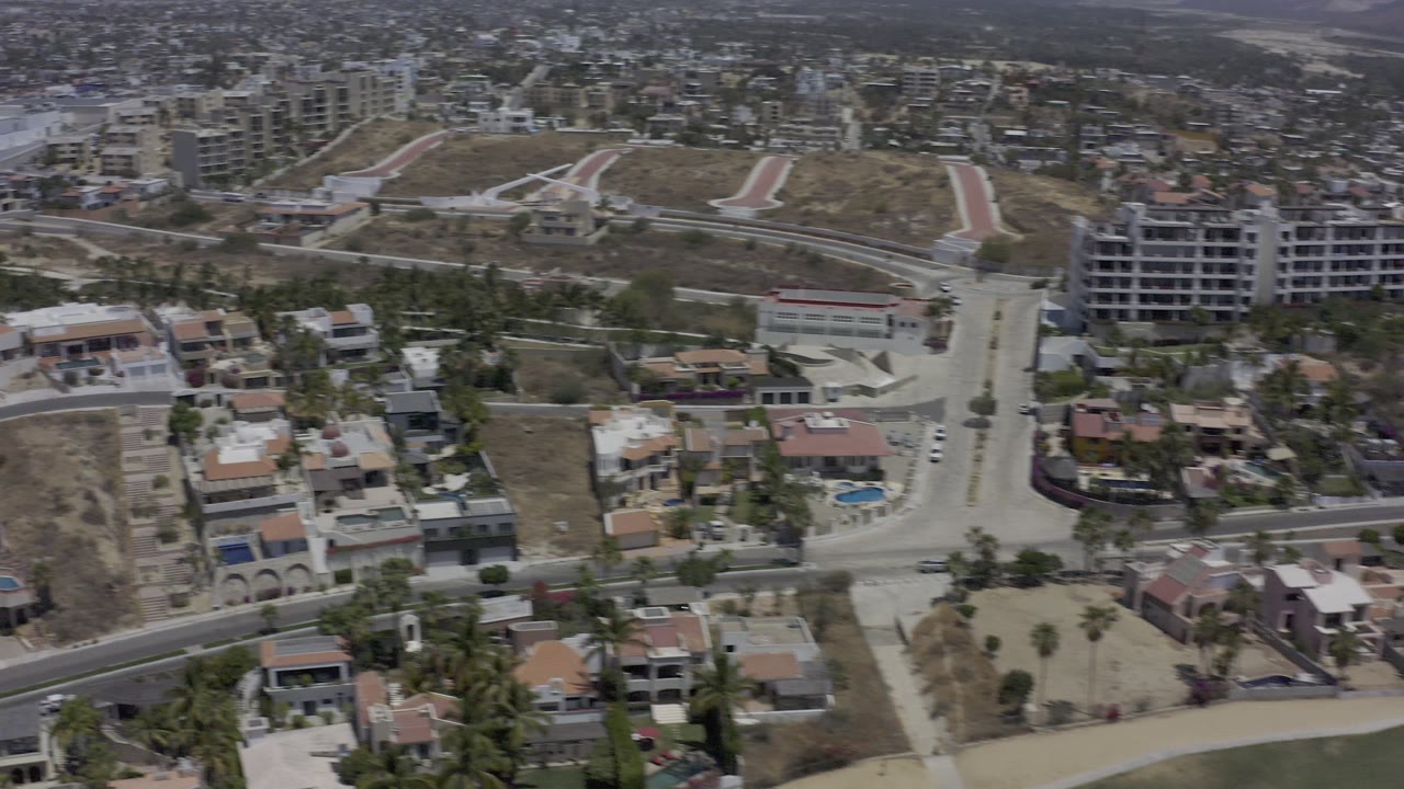 Aerial frame of residential streets, large dry lot, houses, and distant buildings