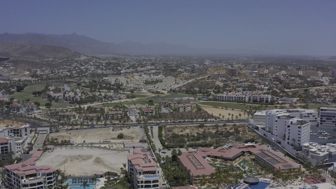 Aerial view over resort buildings, roads, golf greenery, desert lots, and distant hills.