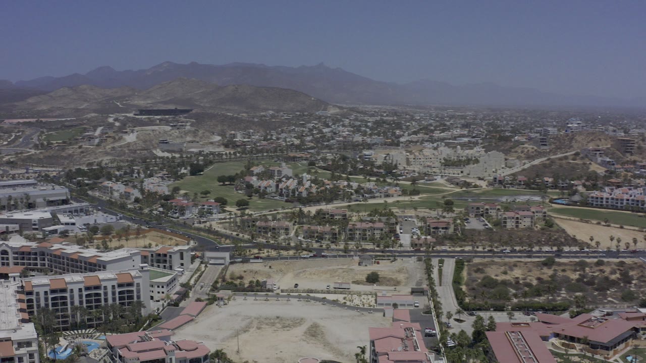 Wide aerial view of resort buildings, roads, desert lots, and distant hills.