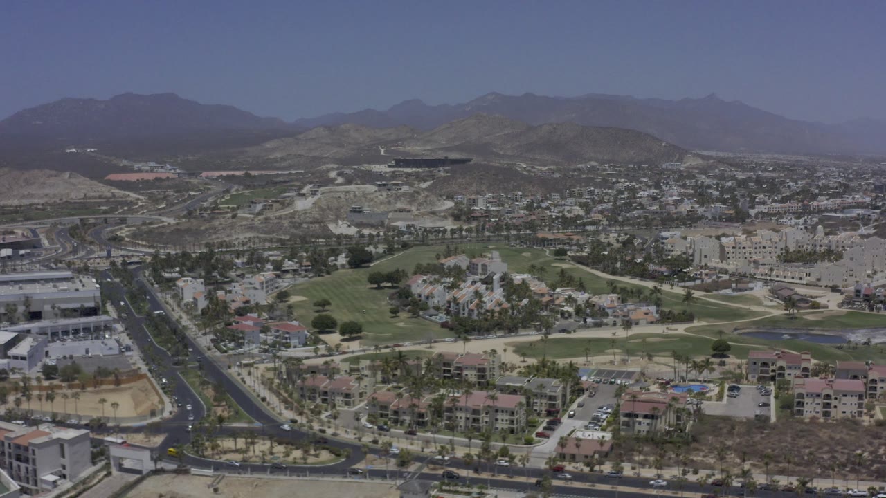 Elevated view of golf-course greens, roads, buildings, and mountains.