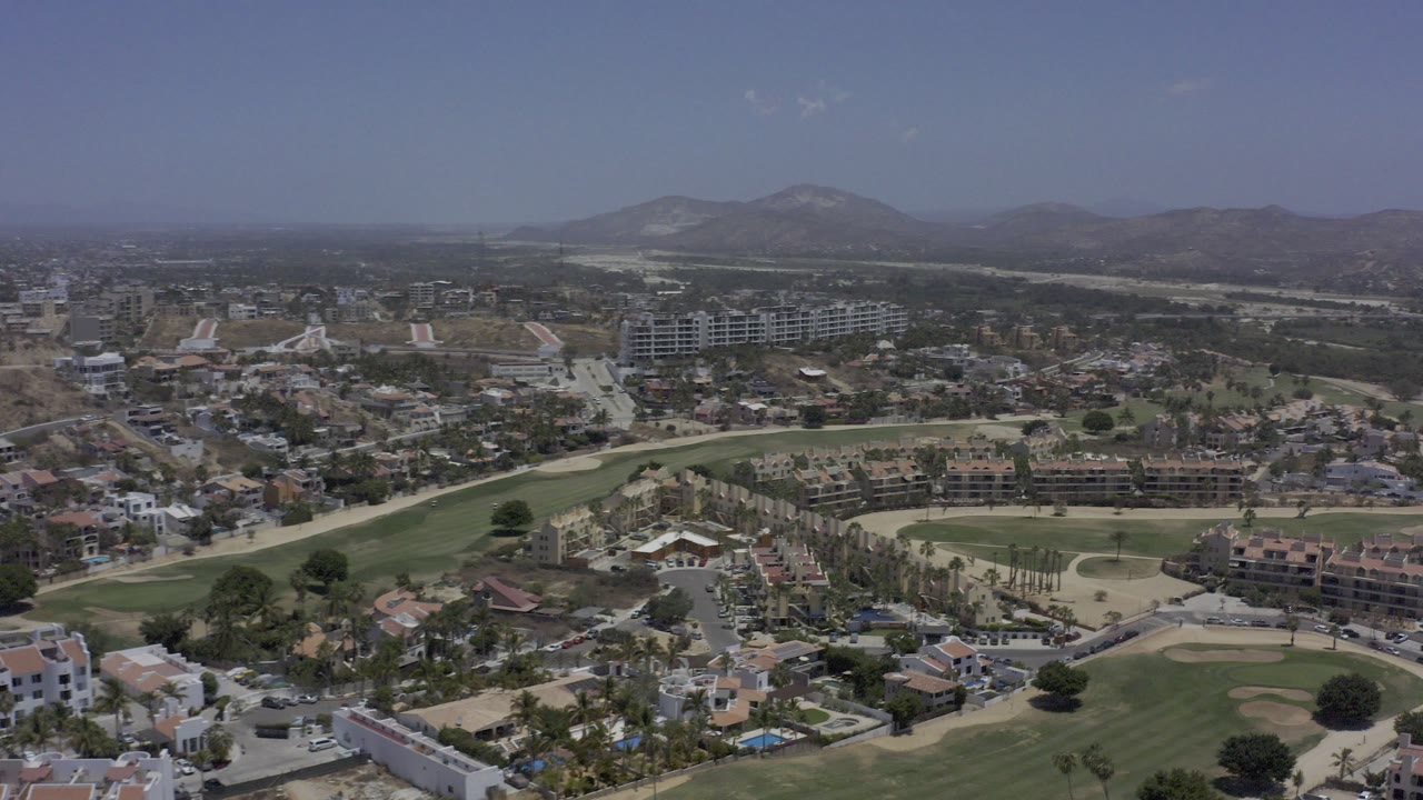 Aerial view of roads, buildings, golf greens, and dry mountains.
