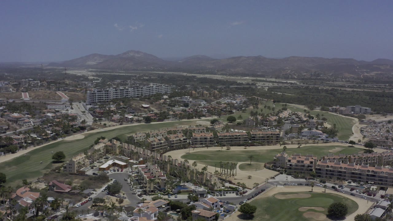 Aerial view over golf course fairways, homes, and hazy hills.