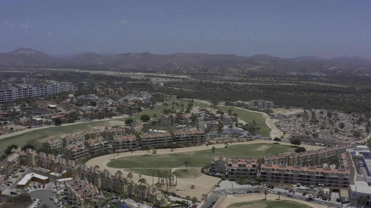 Drone view of apartment blocks, roadways, green lawns, and mountain horizon.