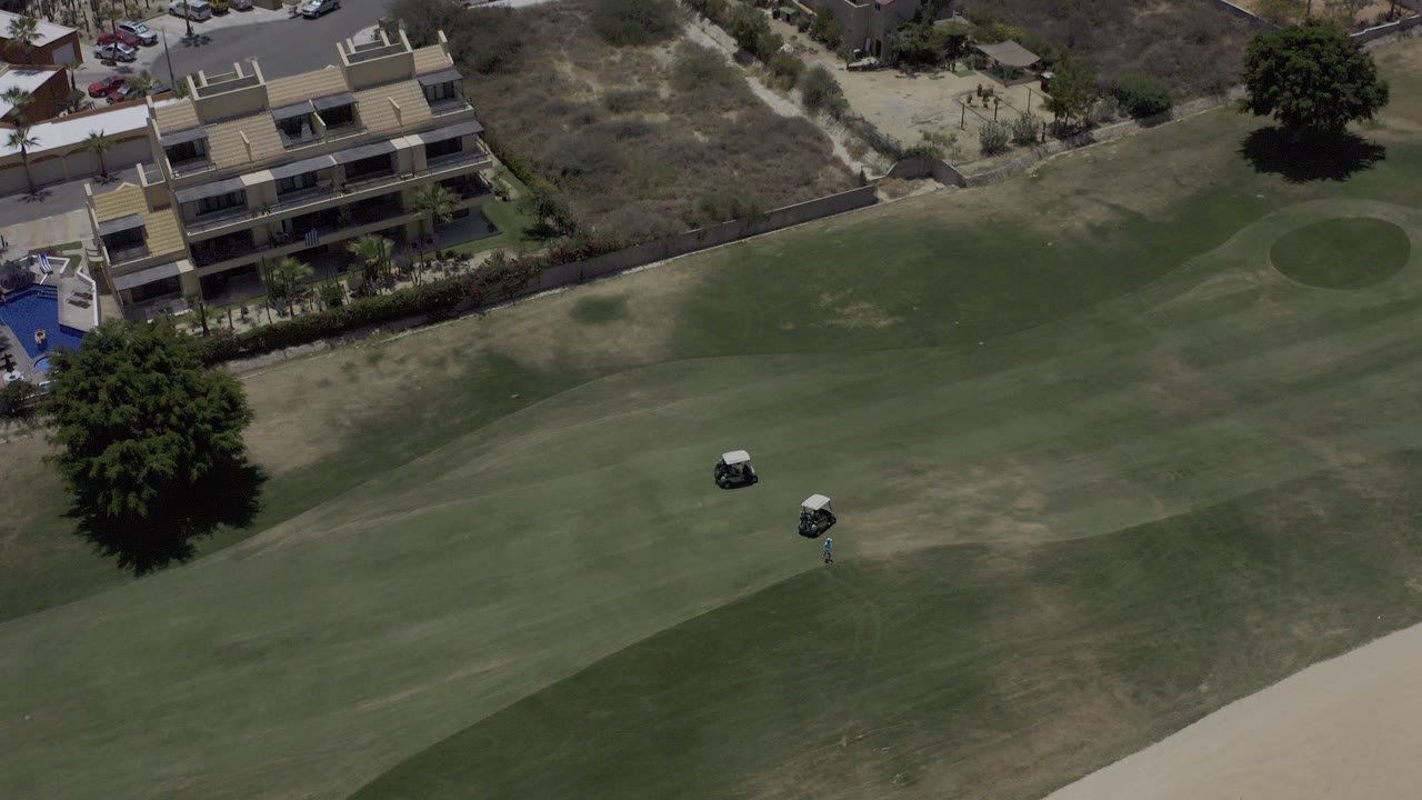 Aerial view of a golf fairway beside condo buildings and dry hillside