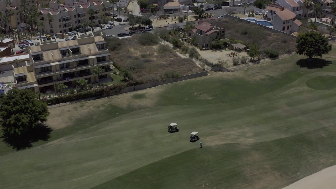 Aerial view of a golf fairway with carts and homes beyond the course.