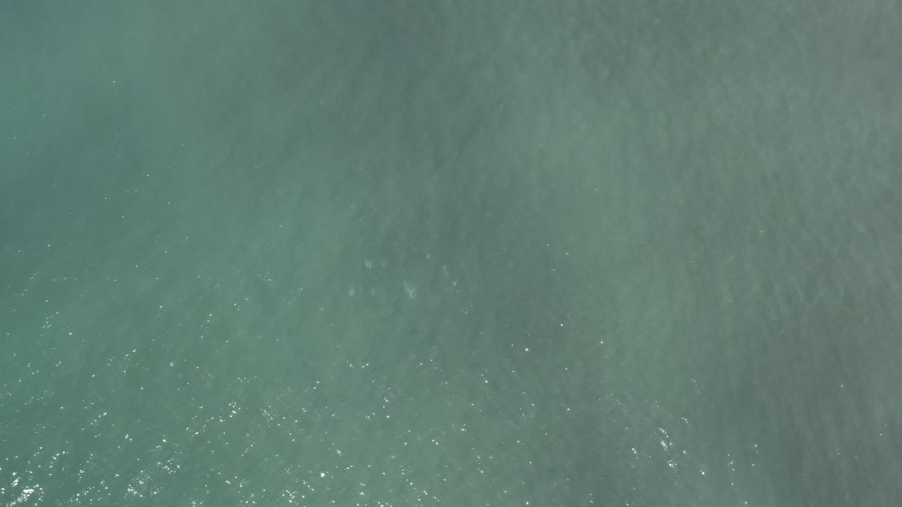 Overhead Los Cabos ocean surface one second in, showing slightly brighter ripple texture across the teal water and no visible people.