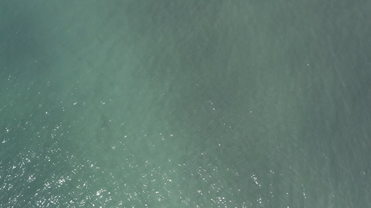 Blue-green water fills the frame in Los Cabos, Mexico, with a broader patch of pale reflections near the center-left and no visible people.