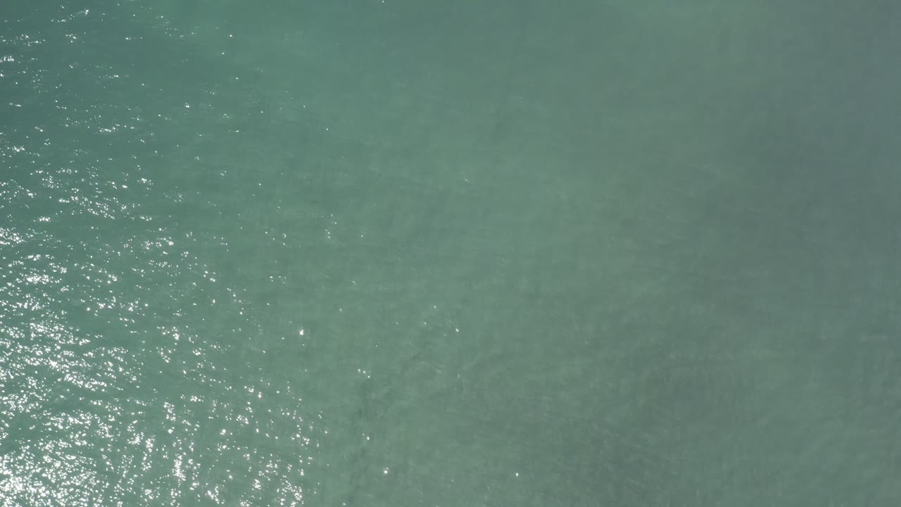 Aerial frame over Los Cabos open water, showing a vertical strip of white sun sparkle near the center and no visible people.