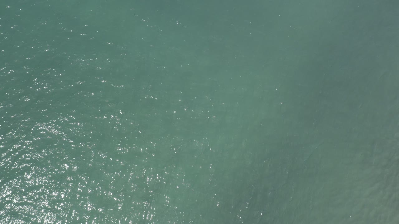 Top-down view of blue-green sea water in Los Cabos, Mexico, with bright sun flecks on the left side and no visible people.