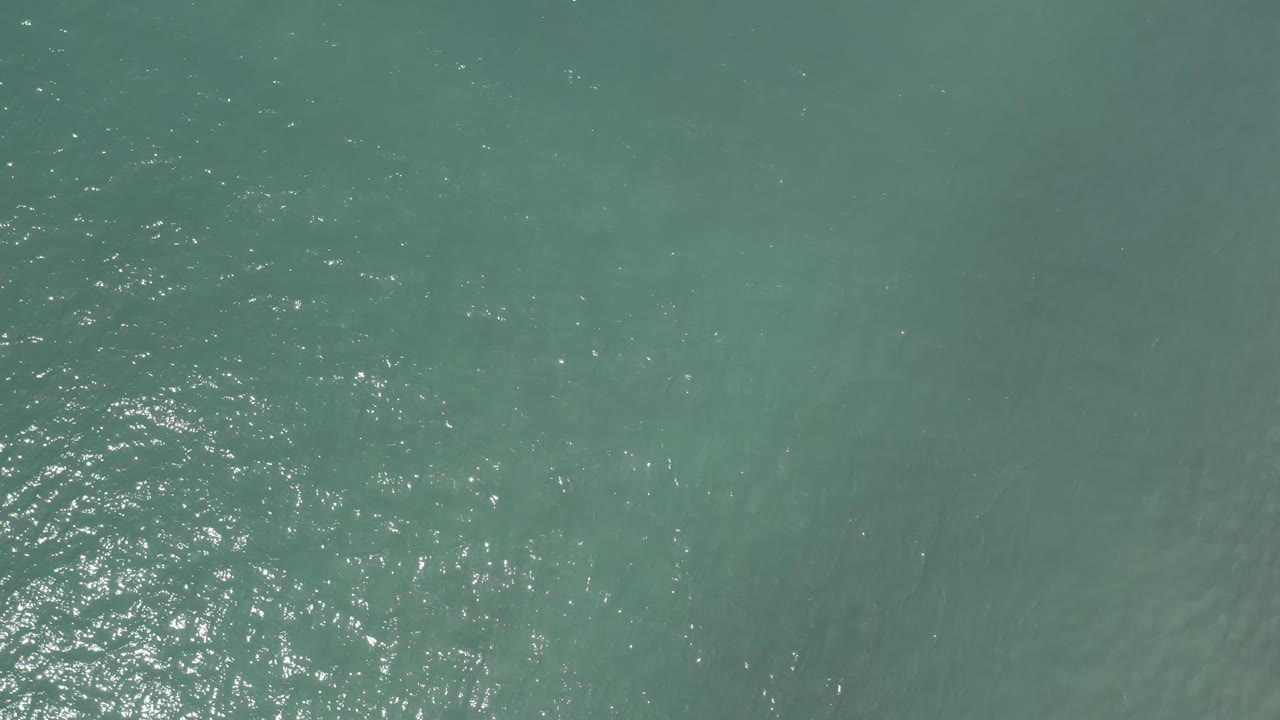 Aerial-looking view of Los Cabos sea water with a brighter column of reflected light near the center and no visible people.