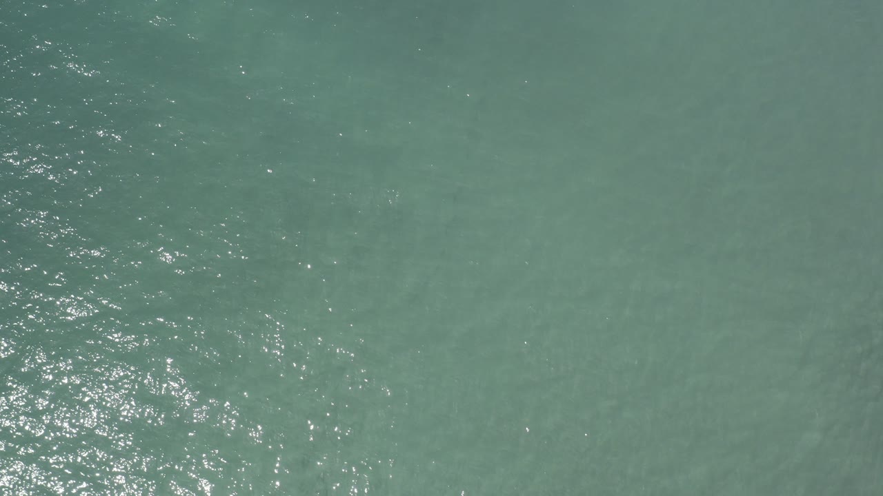 Overhead view of murky green ocean water in Los Cabos, Mexico with bright surface sparkle and no visible people.